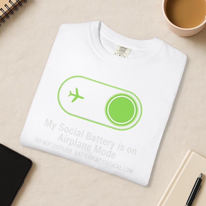 Puede incluir: Camiseta blanca con un avi&oacute;n verde dentro de un dise&ntilde;o de interruptor. El texto dice: "Mi bater&iacute;a social est&aacute; en modo avi&oacute;n. No molestar. Bater&iacute;a baja cr&iacute;tica."
