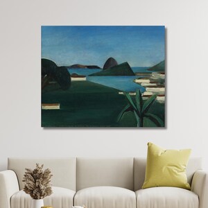 May include: A square canvas print of a landscape painting. The artwork depicts a coastal scene with a dark green foreground, blue water, and a blue sky. The painting is displayed above a beige sofa with a round wooden coffee table.