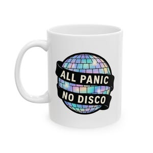 May include: White ceramic mug with a disco ball design and a black banner reading "ALL PANIC NO DISCO". The disco ball has a colourful, iridescent effect. The mug has a curved handle.