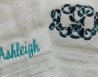 May include: Two white bath towels with embroidered details. One towel features the name "Ashleigh" in teal script. The other towel displays a monogram in teal and black, adding a personalized touch to the soft, absorbent towels.
