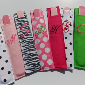 May include: Seven pink nail file holders with different patterns and embroidered letters. The patterns include polka dots, zebra print, and solid pink. The letters are L, M, S, B, K, E, and C.