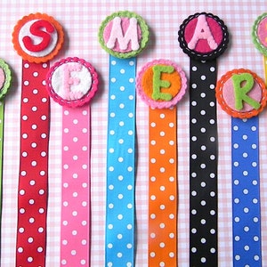 May include: Nine colorful felt letter bookmarks with white polka dot ribbon. The letters spell out the word "SUMMER".