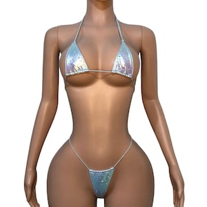 May include: A two-piece bikini set featuring a holographic silver finish with scattered iridescent sparkles. The top consists of two triangular cups with thin halter straps, while the bottom is a high-cut thong style with thin side ties.