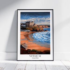 May include: Framed art print of Newquay, England, featuring a coastal landscape. The artwork depicts a beach with blue waves, a sandy shore, and buildings atop a cliff under a cloudy sky. The print is in a black frame and is leaning against a white wall.