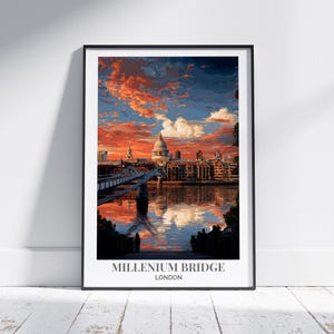May include: Framed art print of the Millennium Bridge in London, with St. Paul's Cathedral in the background. The sky is filled with vibrant orange and blue hues, reflecting in the water below. The print is displayed on a white wall.