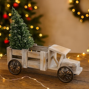 Könnte beinhalten: Ein rustikaler Holzspielzeug-LKW mit einem kleinen grünen Weihnachtsbaum in der Ladefläche. Der LKW hat dunkelbraune Räder und einen hellbraunen Holzrahmen. Der Hintergrund zeigt einen Weihnachtsbaum mit Lichtern.
