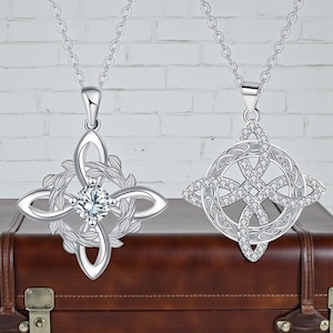 May include: Two silver pendant necklaces. One has a Celtic knot design with a central clear gemstone and leaf accents. The other features a Celtic knot design with embedded clear gemstones. Both hang from delicate chains.