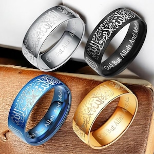 May include: Four rings in silver, black, blue, and gold. Each ring has engraved Arabic script and the phrase "God But Allah And Muha". The rings are displayed on a brown surface.