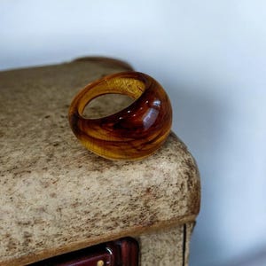 Puede incluir: Un anillo de resina con efecto veteado. El anillo presenta una mezcla de tonos ámbar y marrón oscuro, creando un patrón único y orgánico. El anillo es una pieza audaz, perfecta para añadir un toque artístico a cualquier atuendo.