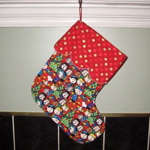 May include: A red and gold Christmas stocking with a red polka dot pattern on the top and a colorful Peanuts character print on the bottom.