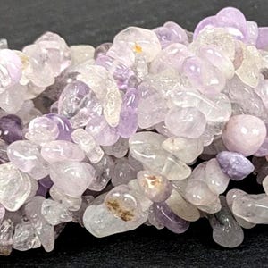 Könnte beinhalten: Nahaufnahme eines Haufens getrommelter Amethyst-Chips. Die Chips variieren in Größe und Form und zeigen Farbtöne von Lavendel, Lila und klarem Quarz. Diese Edelsteine werden oft in Schmuck- und Bastelprojekten verwendet.