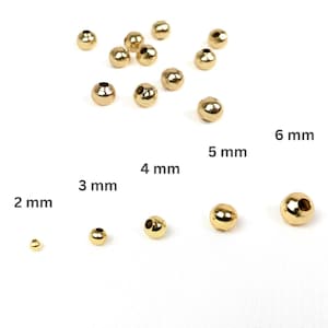 Könnte beinhalten: Goldfarbene Metallperlen in verschiedenen Größen von 2 mm bis 6 mm. Die runden Perlen haben ein Loch in der Mitte, ideal für die Schmuckherstellung oder Bastelarbeiten. Das Bild zeigt die Perlen vor weißem Hintergrund.