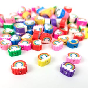 Könnte beinhalten: Eine Sammlung bunter Polymer Clay Perlen. Die Perlen sind in Form von Regenbogen und Wolken gehalten, mit einem Loch zum Auffädeln. Die Farben umfassen Rot, Gelb, Grün, Blau, Rosa und Lila. Ideal für Schmuckherstellung und Bastelarbeiten.