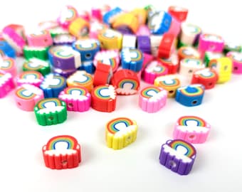 Könnte beinhalten: Eine Sammlung bunter Polymer Clay Perlen. Die Perlen sind in Form von Regenbogen und Wolken gehalten, mit einem Loch zum Auffädeln. Die Farben umfassen Rot, Gelb, Grün, Blau, Rosa und Lila. Ideal für Schmuckherstellung und Bastelarbeiten.