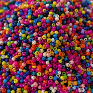 Könnte beinhalten: Nahaufnahme eines Haufens kleiner, bunter Perlen. Die Perlen sind eine Mischung aus leuchtenden Farben, darunter Pink, Orange, Gelb, Blau und Grün. Sie sind rund mit einem Loch in der Mitte, ideal für Schmuckherstellung oder Bastelarbeiten.