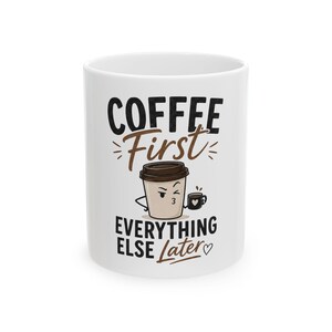 May include: A white ceramic mug featuring the black and brown text COFFEE First EVERYTHING ELSE Later. The design includes a cartoon coffee cup character with a winking face holding a smaller black mug with a white heart icon on its side.
