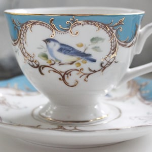 May include: A blue and white teacup and saucer set with a gold trim and a bluebird design.