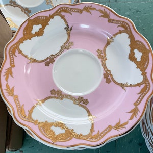 K&ouml;nnte beinhalten: Ein Set aus rosa und wei&szlig;en Porzellan-Teetassen und Untertassen mit goldenen Verzierungen und filigranen Blumendesigns.
