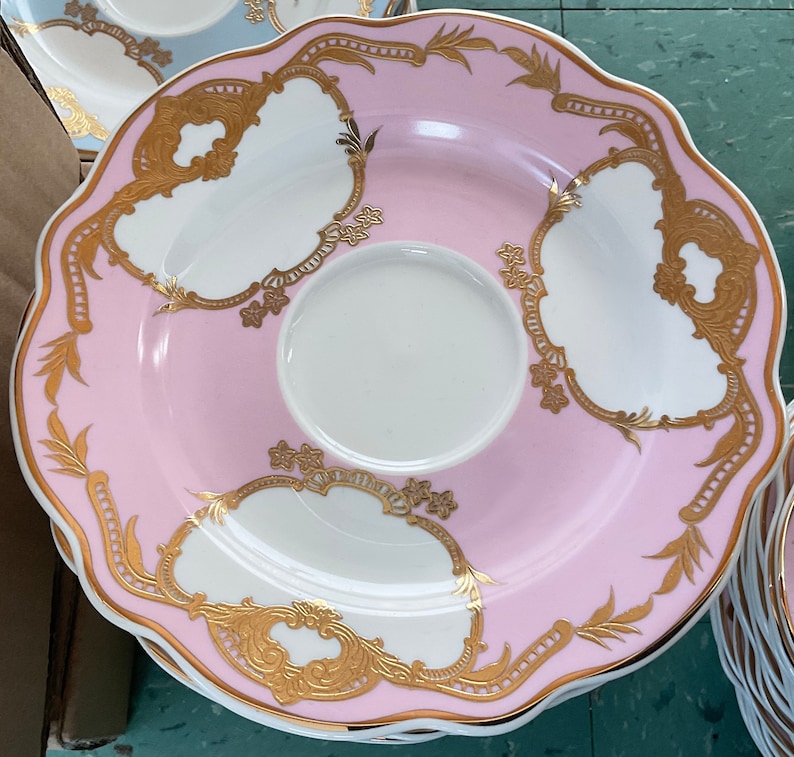 K&ouml;nnte beinhalten: Ein Set aus rosa und wei&szlig;en Porzellan-Teetassen und Untertassen mit goldenen Verzierungen und filigranen Blumendesigns.