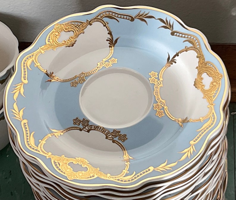K&ouml;nnte beinhalten: Ein Stapel blauer und wei&szlig;er Porzellansaucers mit goldenen Verzierungen und filigranen Blumendesigns. Die Untertassen haben einen gewellten Rand und eignen sich perfekt zum Servieren von Tee oder Kaffee.