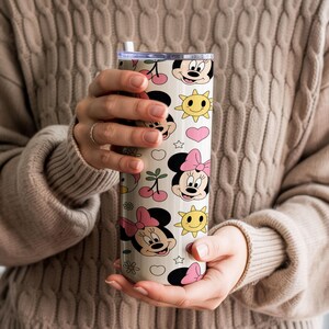 Pu&ograve; includere: Un bicchiere cilindrico con sfondo color crema caratterizzato da un motivo ripetuto di volti di Minnie, fiocchi rosa, soli gialli, ciliegie rosse, cuori rosa e piccole stelle bianche. Il bicchiere include un coperchio trasparente e una cannuccia bianca.