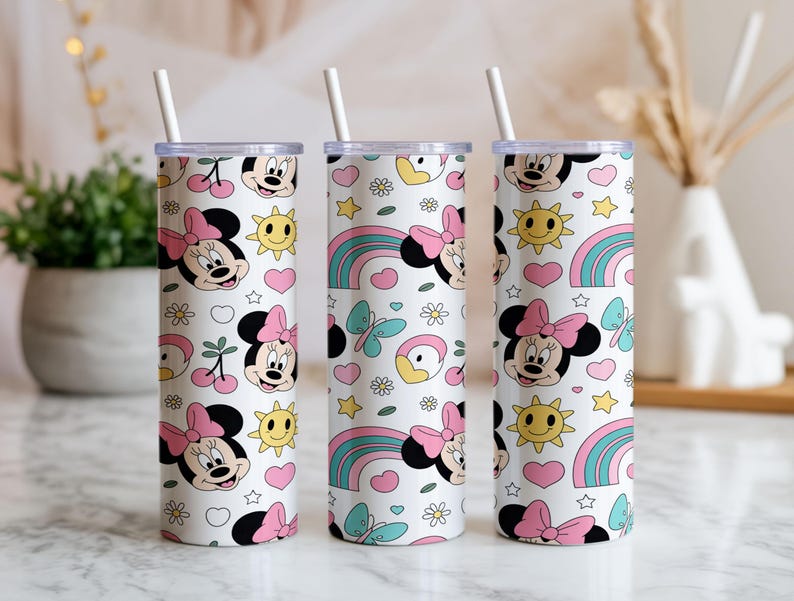 Pu&ograve; includere: Tre bicchieri cilindrici bianchi con coperchi trasparenti e cannucce bianche, ciascuno caratterizzato da un motivo ripetuto di volti di Minnie con fiocchi rosa, soli gialli, cuori rosa, arcobaleni blu, piccoli fiori bianchi e farfalle azzurre.