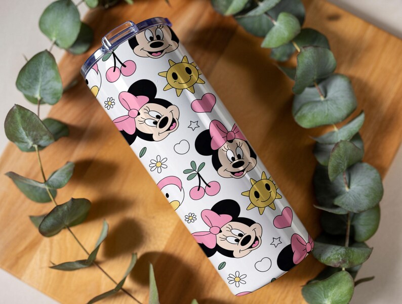 Pu&ograve; includere: Un bicchiere cilindrico bianco con un motivo ripetuto di volti di Minnie con fiocchi rosa, soli gialli sorridenti, ciliegie rosa, piccoli fiori bianchi e cuori rosa, dotato di un coperchio in plastica trasparente.