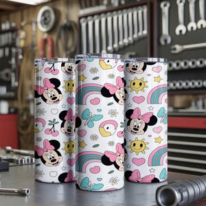 Pu&ograve; includere: Tre bicchieri cilindrici con un motivo ripetuto su sfondo bianco. Il design include volti di Minnie con fiocchi rosa, arcobaleni colorati, soli gialli, farfalle blu, cuori rosa, piccoli fiori bianchi e ciliegie.