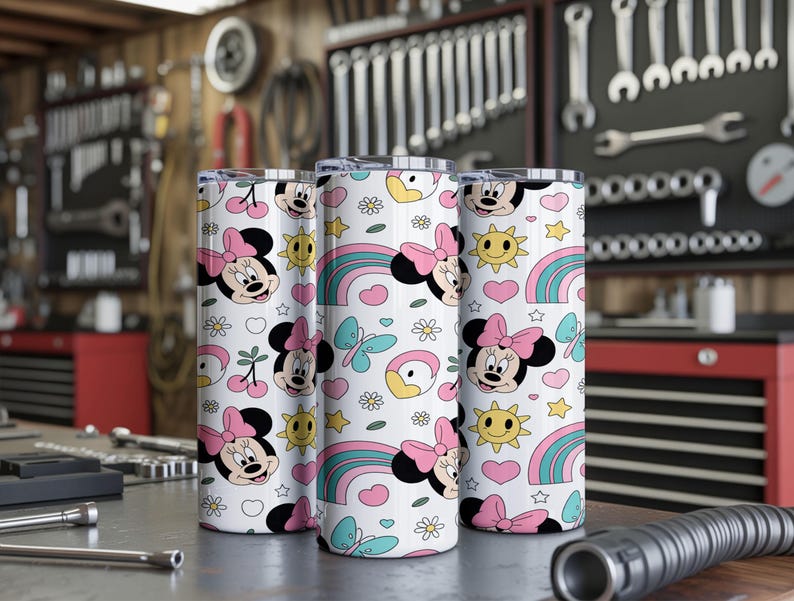 Pu&ograve; includere: Tre bicchieri cilindrici con un motivo ripetuto su sfondo bianco. Il design include volti di Minnie con fiocchi rosa, arcobaleni colorati, soli gialli, farfalle blu, cuori rosa, piccoli fiori bianchi e ciliegie.