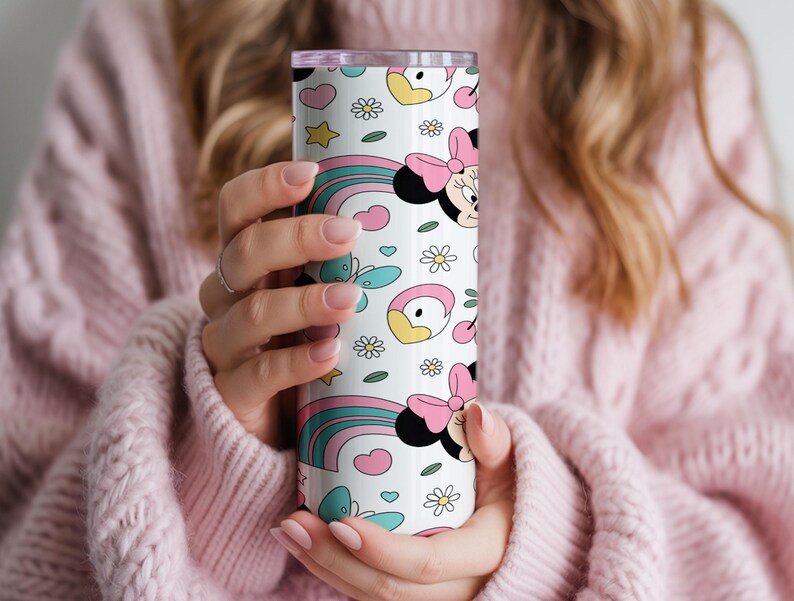 Pu&ograve; includere: Un bicchiere cilindrico in acciaio inossidabile con sfondo bianco e un motivo ripetuto di teste di Minnie Mouse, fiocchi rosa, arcobaleni colorati, farfalle color ottanio, stelle gialle, piccoli cuori e margherite bianche.