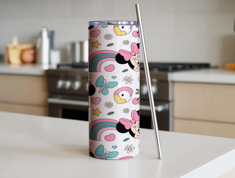 Pu&ograve; includere: Un bicchiere cilindrico con coperchio trasparente e cannuccia in metallo, caratterizzato da un motivo ripetuto su sfondo rosa chiaro. Il design include teste di topo con fiocchi rosa, arcobaleni colorati, farfalle azzurre e fiori bianchi.