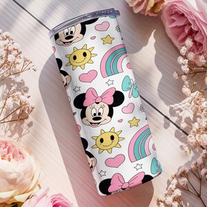 Pu&ograve; includere: Un bicchiere cilindrico bianco con un motivo ripetuto di volti di Minnie con fiocchi rosa, soli gialli sorridenti, cuori rosa, arcobaleni color ottanio e rosa, piccole stelle e farfalle color ottanio, dotato di un coperchio trasparente.