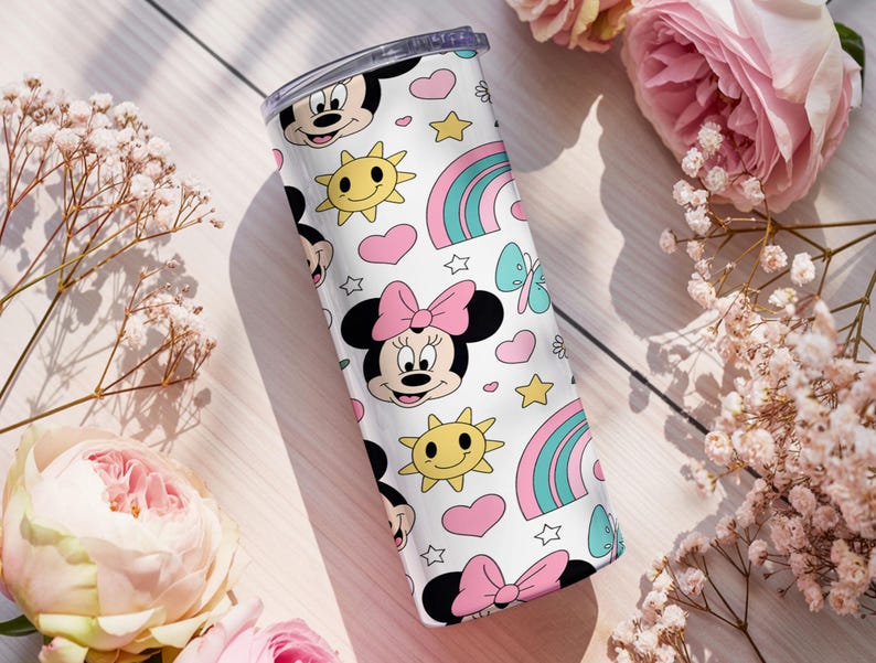 Pu&ograve; includere: Un bicchiere cilindrico bianco con un motivo ripetuto di volti di Minnie con fiocchi rosa, soli gialli sorridenti, cuori rosa, arcobaleni color ottanio e rosa, piccole stelle e farfalle color ottanio, dotato di un coperchio trasparente.
