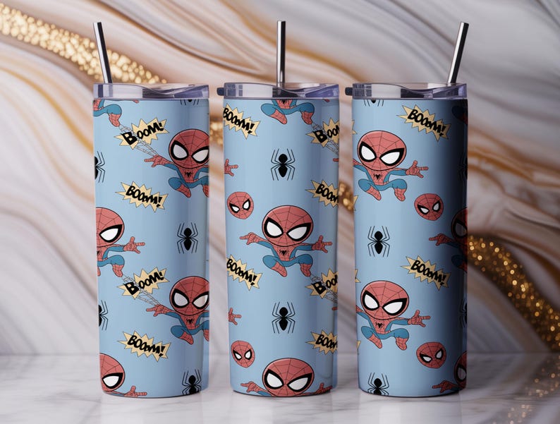 May include: Three stainless steel tumblers with lids and straws. Each tumbler features a light blue background with a repeating pattern of Spider-Man illustrations, spider webs, and the word "BOOM!" in yellow speech bubbles.