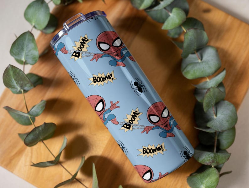May include: A light blue tumbler featuring a repeating pattern of the Spider-Man character in action poses, along with the word "BOOM!" in yellow starbursts and black spider icons. The tumbler has a silver lid.