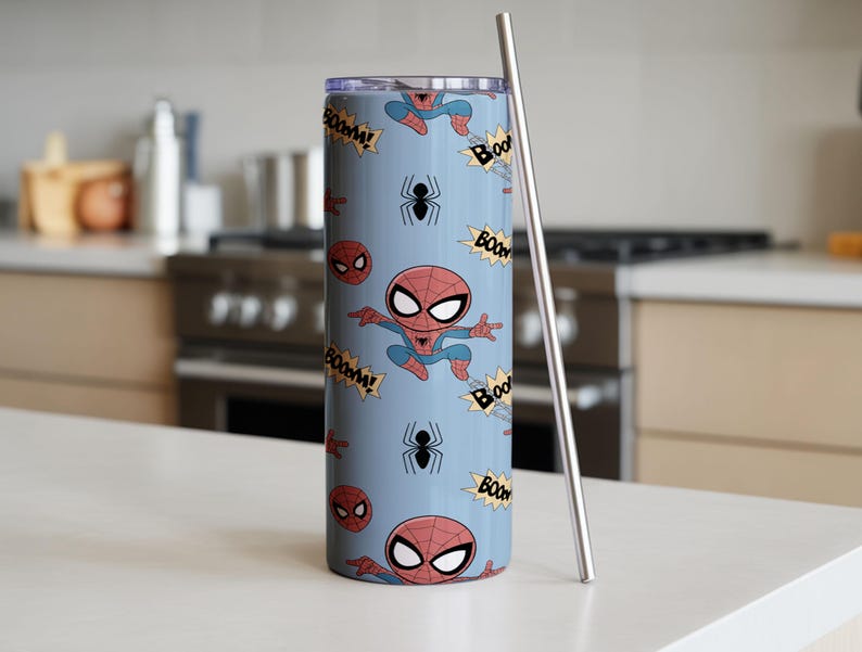 May include: A light blue tumbler with a Spider-Man cartoon pattern. The design includes Spider-Man figures, spider webs, and "BOOM!" text. A silver-colored metal straw is placed next to the tumbler. The tumbler is cylindrical and appears to be made of stainless steel.