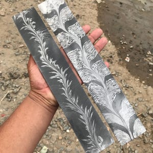 Può includere: Due lastre rettangolari con una base grigio scuro e intricati motivi bianchi a forma di piuma. La lastra sinistra mostra un design a piuma centrale singola, mentre quella destra presenta una serie di motivi ripetuti a forma di foglia.
