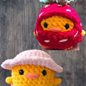 May include: Two crocheted chick toys. One is yellow with a pink hat. The other is yellow with a red strawberry costume. Both have black eyes and orange beaks. The toys are handmade.