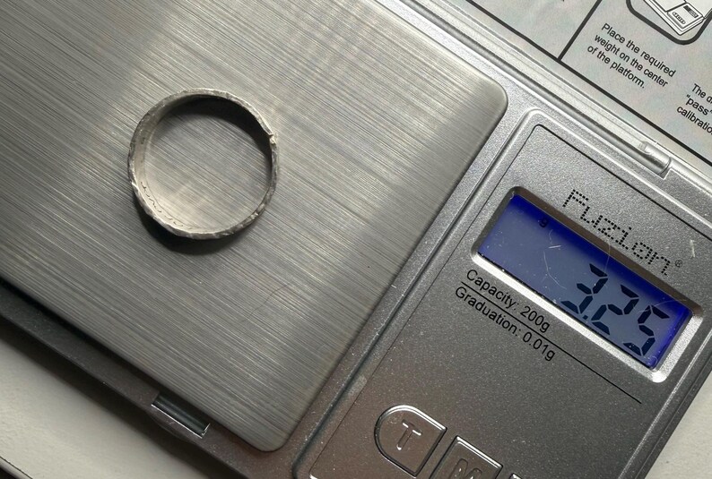 May include: A silver-toned metal ring with a textured, uneven surface resting on a digital scale. The scale display shows a weight of 3.25 grams. The scale is a Fuzion brand model with a 200-gram capacity and 0.01-gram graduation increments.