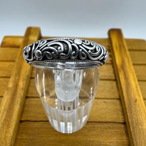 May include: A silver ring featuring an intricate, raised scrollwork pattern with oxidized recessed areas. The band has a rounded profile and a polished finish on the relief details, showcasing a continuous swirling design around the entire circumference.
