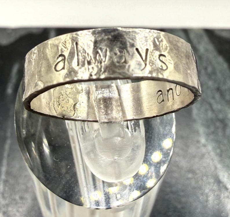 May include: A silver-toned metal ring with a hammered, textured surface. The word "always" is stamped in lowercase letters across the front outer band, while the word "and" is partially visible on the right side of the inner band surface.