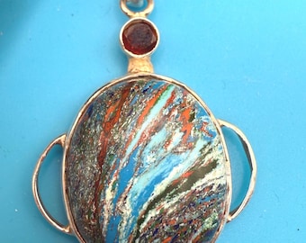 May include: A silver pendant with a large, round, multicolored stone. The stone features streaks of blue, orange, and green. A small, round, red stone sits above the larger stone. The pendant has a silver loop at the top.