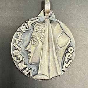 May include: A silver-toned pendant with the words "VIRGO MARIA" and "OPEN" encircling a profile of a woman wearing a veil. The pendant has a loop at the top for a chain.