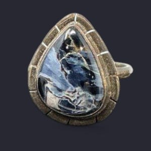 May include: A silver-toned ring with a teardrop-shaped stone. The stone features a swirling pattern of blue and white, set within a textured, silver-colored bezel. The ring band is a simple, rounded design.