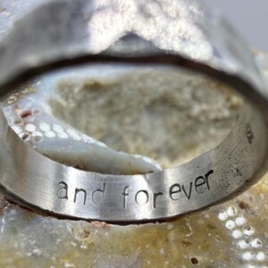 May include: A silver-toned metal ring with a hammered, textured exterior surface. The interior of the band features the engraved lowercase text "and forever" in a simple, sans-serif font. The ring has a wide, substantial band construction.