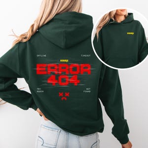 Puede incluir: Sudadera con capucha verde oscuro con el texto "ERROR 404" en rojo, con la marca "KINOJI" en amarillo. La sudadera también presenta las frases "OFFLINE", "TIMEOUT", "TRY AGAIN" y "NOT FOUND".