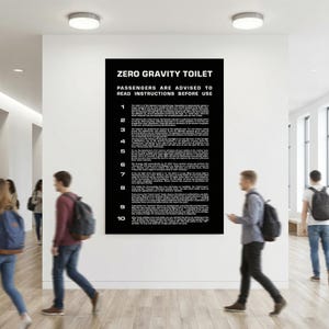 Könnte beinhalten: Ein großes schwarzes rechteckiges Plakat an einer weißen Wand mit weißem Text unter der Überschrift ZERO GRAVITY TOILET. Der Text enthält zehn nummerierte Anweisungen, die vor der Benutzung zu lesen sind und das Toilettensystem erklären.