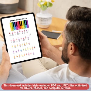 May include: A person holding a tablet displaying a colorful piano key chart for "Carol of the Bells." The chart uses color-coded notes and musical notation. The bottom of the tablet reads: "This download includes high-resolution PDF and JPEG files..."