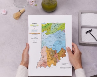 Op de afbeelding: Een persoon houdt een kleurrijke kaart van Indiana vast, met verschillende regio's in groen, geel, blauw en oranje. De kaart is gedetailleerd met tekst en geografische kenmerken. Een glas groene vloeistof en een kleine zen-tuin zijn op de achtergrond.