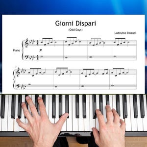 Op de afbeelding: Een bladmuziekpagina getiteld Giorni Dispari (Odd Days) van Ludovico Einaudi voor piano, met zwarte muzieknotatie op een witte achtergrond, geplaatst boven een pianotoetsenbord met zwarte en witte toetsen en handen die op de toetsen rusten.
